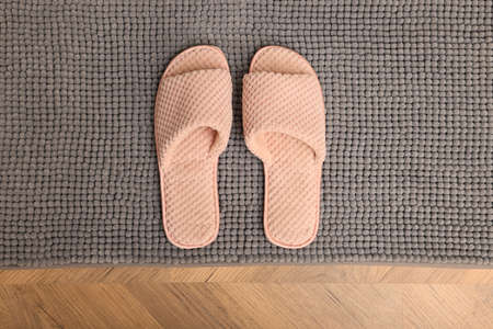 Soft gray bath mat and slippers on floor, top view