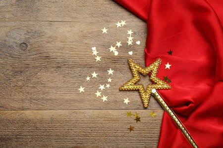 Beautiful golden magic wand, confetti and red fabric on wooden table, top view. Space for text