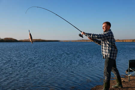 Fisherman catching fish with rod at riverside