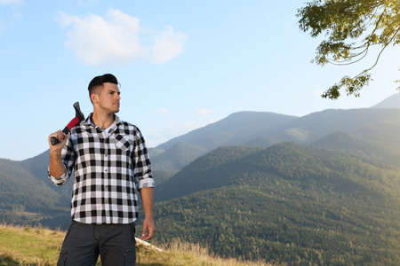 Handsome man with ax in mountains, space for textの写真素材