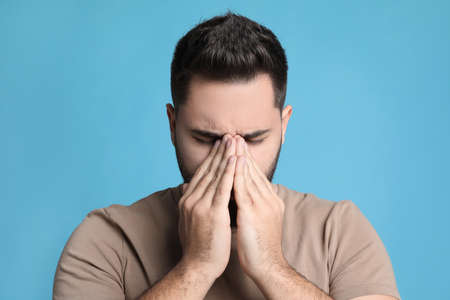 Young man suffering from headache on light blue backgroundの写真素材