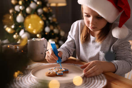 Little child in Santa hat decorating Christmas cookie at wooden table indoorsの写真素材