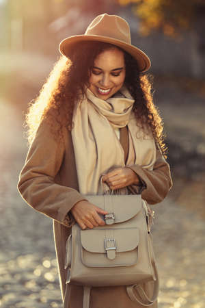 Beautiful African-American woman with stylish beige backpack on autumn dayの写真素材