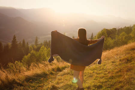 Woman with cozy plaid enjoying warm sunlight in mountains, back viewの写真素材