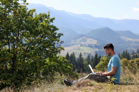 Man working with laptop outdoors surrounded by beautiful nature. Space for text