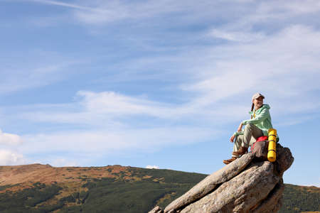 Young woman with backpack and sleeping mat on cliff in mountains. Space for textの写真素材