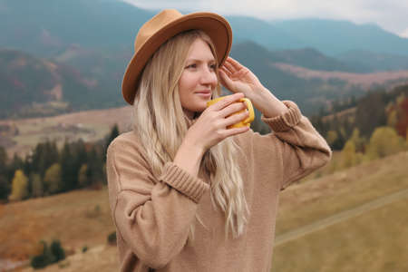 Young woman with mug of hot drink in mountains. Space for textの写真素材