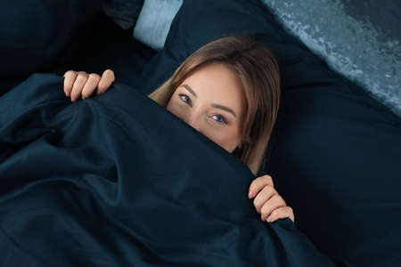 Young woman in comfortable bed with dark blue linens, above viewの写真素材