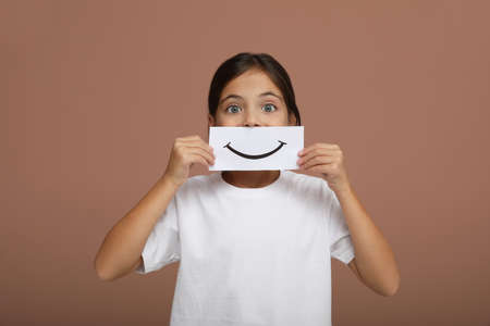 Little girl holding sheet of paper with smile on pale pink backgroundの写真素材