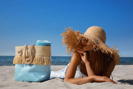 Woman with beach bag and straw hat lying on sand near seaの写真素材