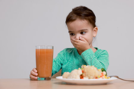 Cute little girl covering mouth and refusing to drink juice at table on gray backgroundの写真素材