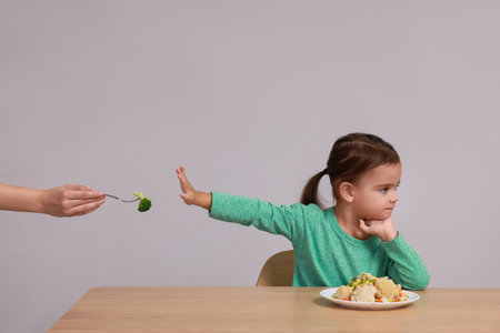 Cute little girl refusing to eat vegetables at table on gray backgroundの写真素材