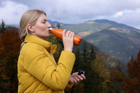 Young woman drinking hot beverage from thermo bottle in mountainsの写真素材
