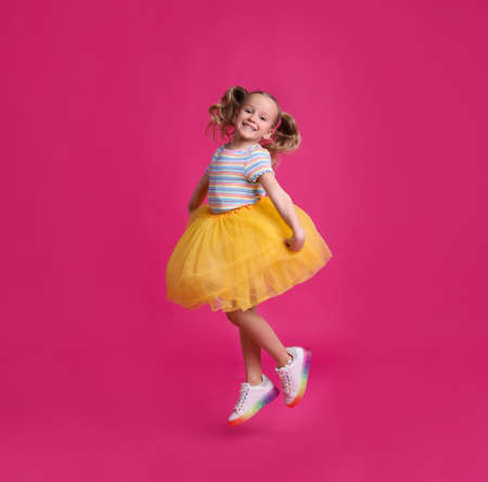 Cute little dancer in tutu skirt jumping on pink backgroundの写真素材