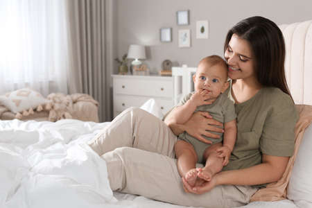 Happy young mother with her cute baby on bed at home