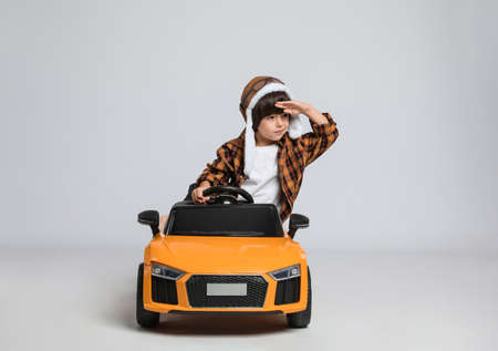 Cute little boy in pilot hat driving children's electric toy car on gray backgroundの写真素材