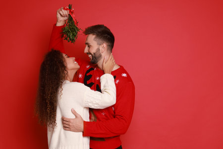 Lovely couple under mistletoe bunch on red background. Space for textの写真素材