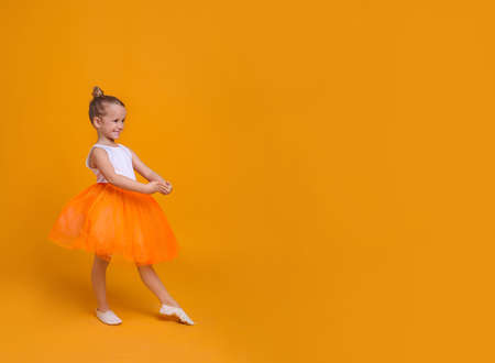 Cute little girl in tutu skirt dancing on orange background. space for textの写真素材