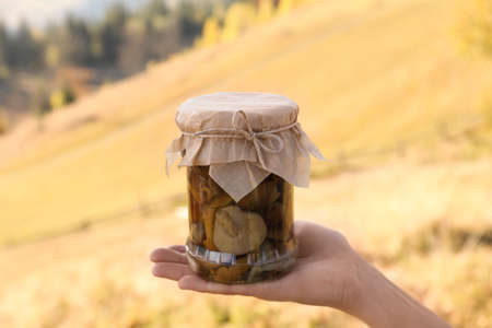 Woman holding glass jar with pickled mushrooms outdoors, closeupの写真素材