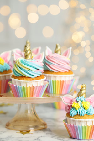 Cute sweet unicorn cupcakes on white marble table against blurred lightsの写真素材
