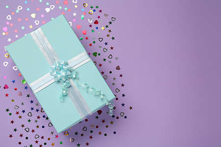 Light blue gift box and sequins on lilac background, flat lay. Space for textの写真素材