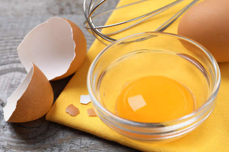 Bowl with raw egg yolk on gray wooden table, closeup