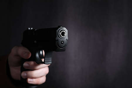 Man aiming gun against dark background, closeup. Space for textの写真素材