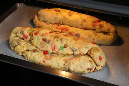 Raw homemade Stollens with candied fruits and nuts on baking tray in oven, closeup. Traditional German Christmas breadの写真素材