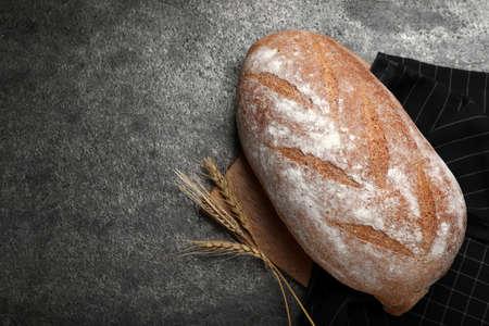 Loaf of tasty sodawater bread and wheat spikes on gray table, flat lay. Space for textの写真素材