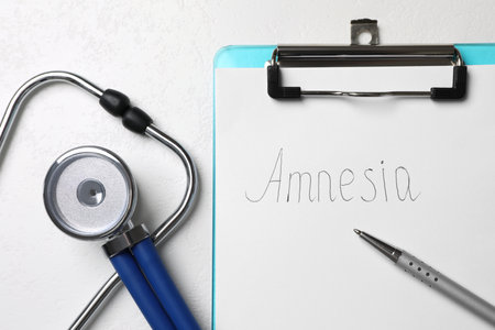Clipboard with word Amnesia, pen and stethoscope on white table, flat layの写真素材