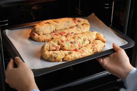 Woman putting baking tray with raw homemade Stollens into oven, closeup. Traditional German...