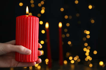 Woman holding burning red candle against blurred Christmas lights, closeup. Space for textの写真素材