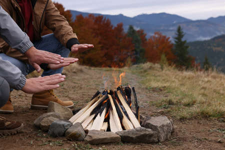 Men warming hands near bonfire outdoors, closeup. Camping seasonの写真素材