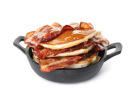 Delicious pancakes with maple syrup and fried bacon in frying pan on white backgroundの写真素材