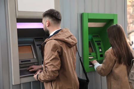 Young man using cash machine for money withdrawal outdoorsの写真素材