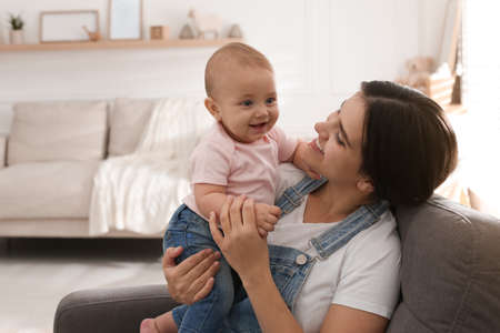 Happy young mother with her cute baby in armchair at home