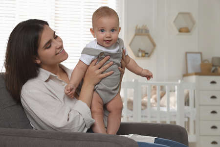 Happy young mother with her baby in armchair at home