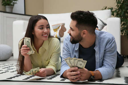 Happy couple with money on floor at homeの写真素材