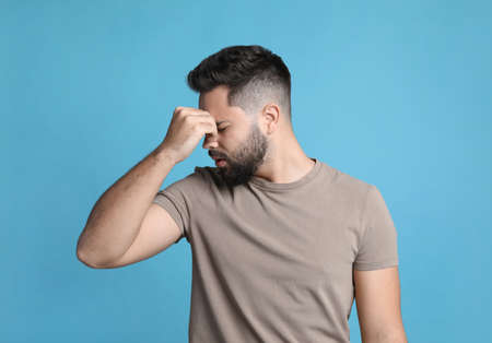 Young man suffering from headache on light blue backgroundの写真素材