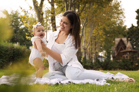 Happy mother with adorable baby sitting on green grass in park