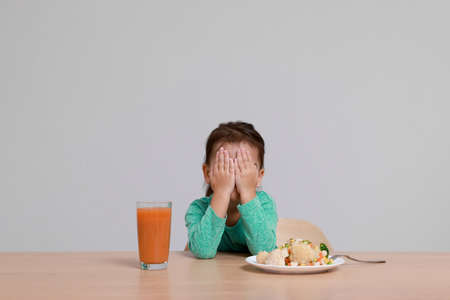 Cute little girl crying and refusing to eat vegetable salad at table on gray backgroundの写真素材