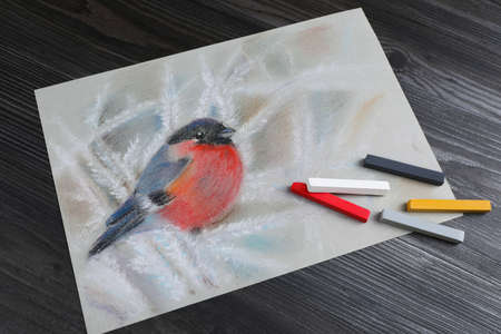 Colorful chalk pastels and beautiful painting of bullfinch on black wooden table, above viewの写真素材