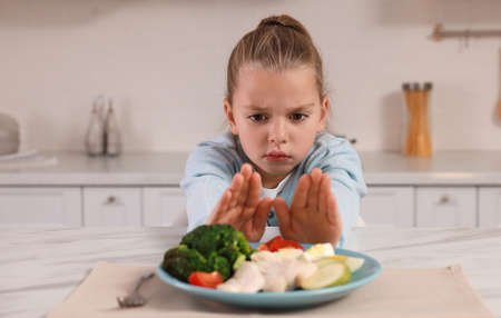 Cute little girl refusing to eat dinner in kitchenの写真素材