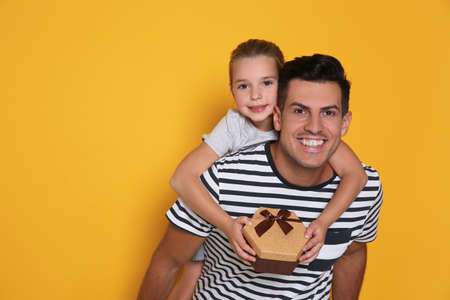 Man receiving Father's Day gift from his daughter on yellow background. Space for textの写真素材