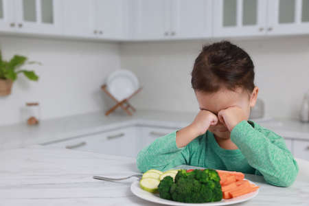 Cute little girl crying and refusing to eat vegetables in kitchen, space for textの写真素材