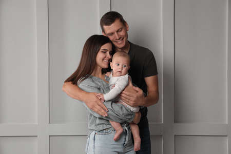 Happy family. Couple with their cute baby near light wall