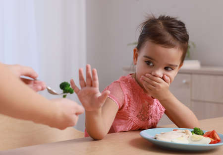 Cute little girl covering her mouth and refusing to eat breakfast at homeの写真素材