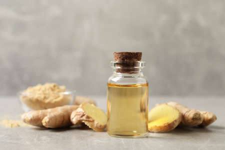 Glass bottle of essential oil and ginger root on gray tableの写真素材