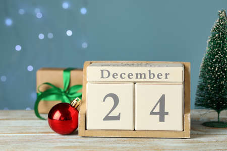 December 24 - Christmas Eve. Wooden block calendar and decor on table against blurred festive lights