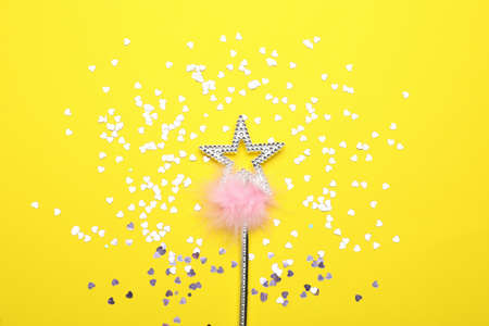 Beautiful silver magic wand with feather and confetti on yellow background, flat lay